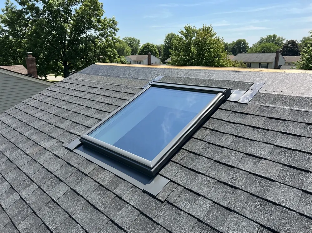 New fixed skylight with metal flashing set into a dark asphalt shingle roof